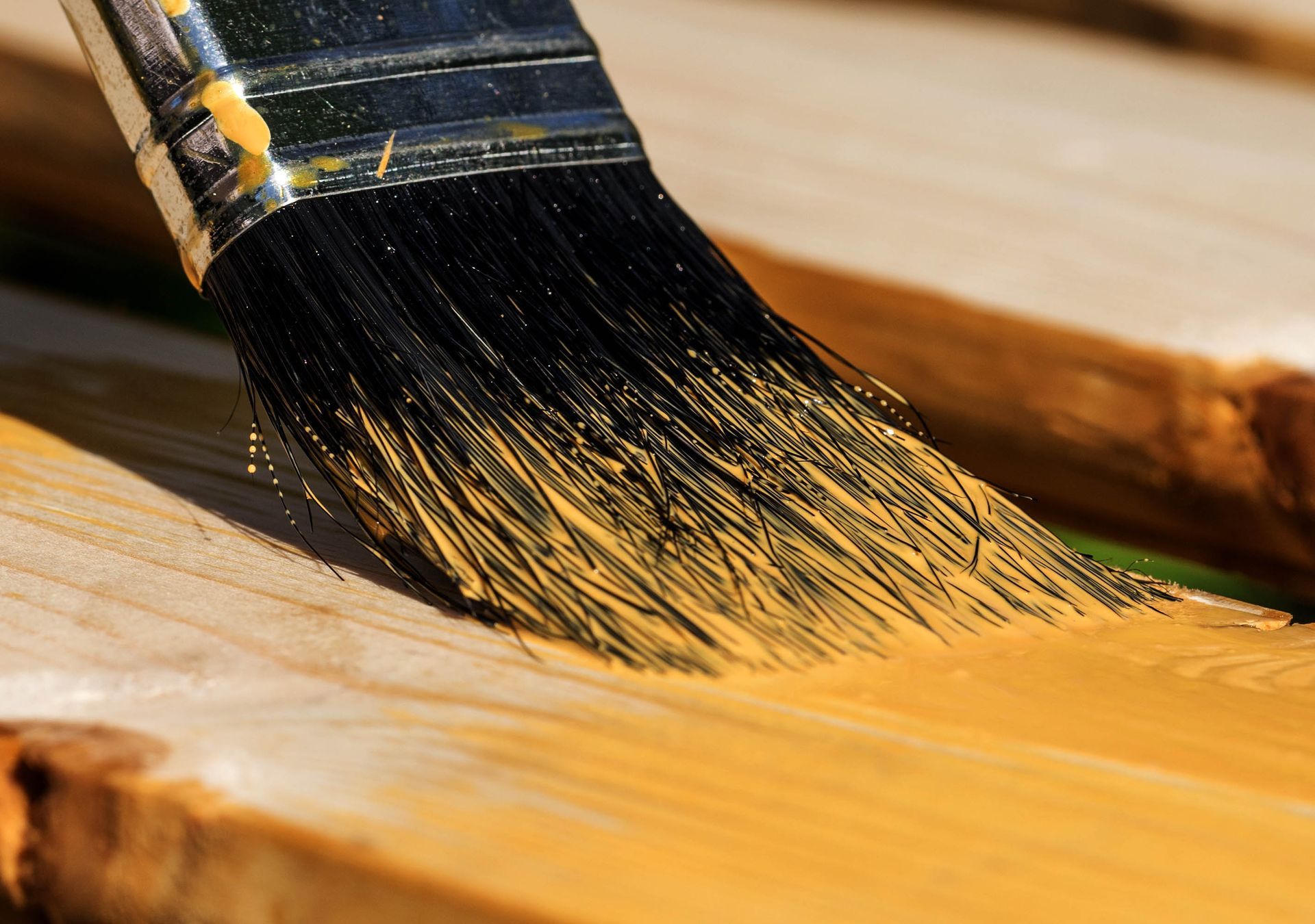 Pinsel zum Auftragen gelber Beize auf Holzplanken.