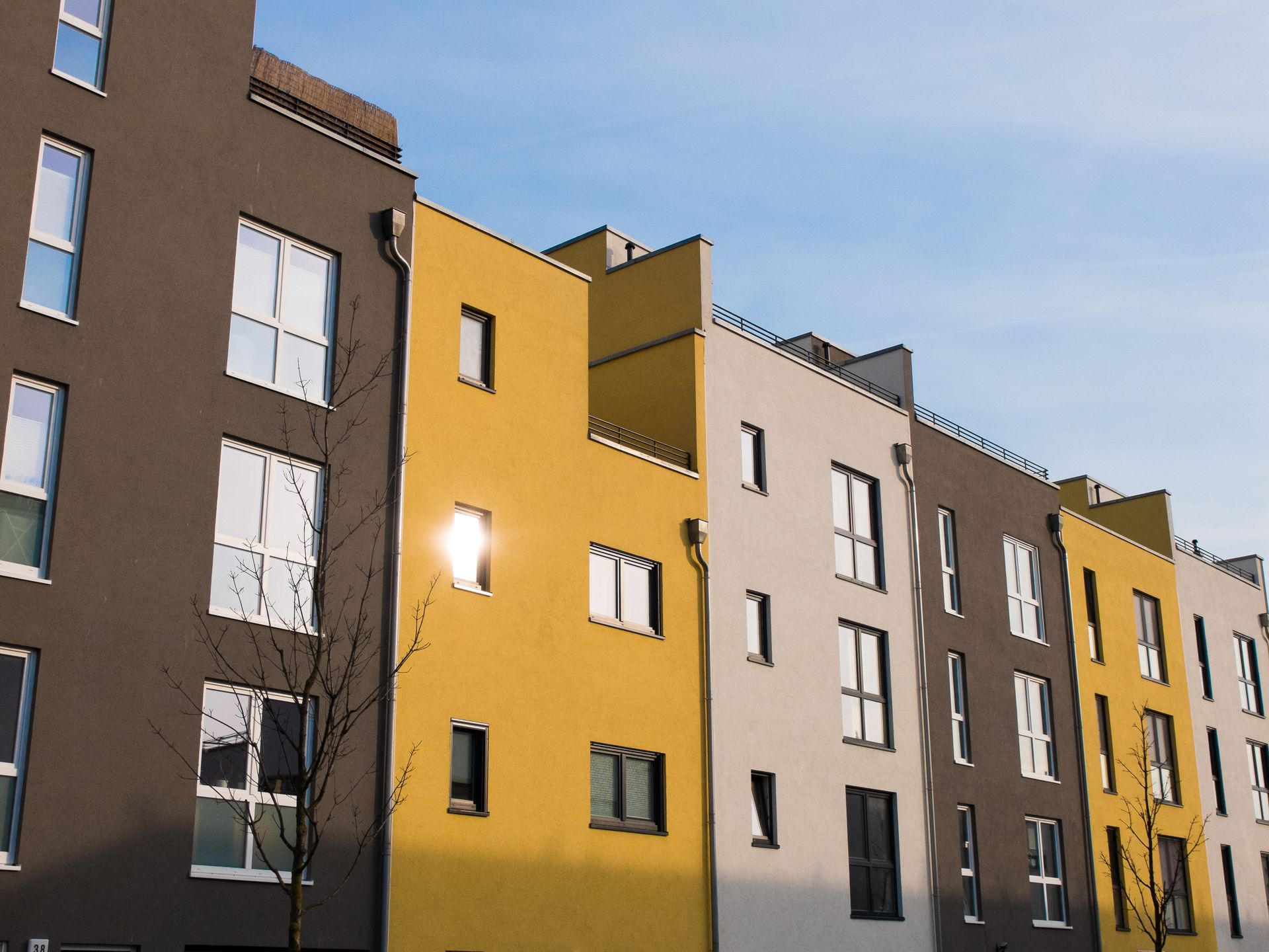 Eine Reihe moderner Wohnhäuser mit gelben, grauen und braunen Fassaden unter blauem Himmel.