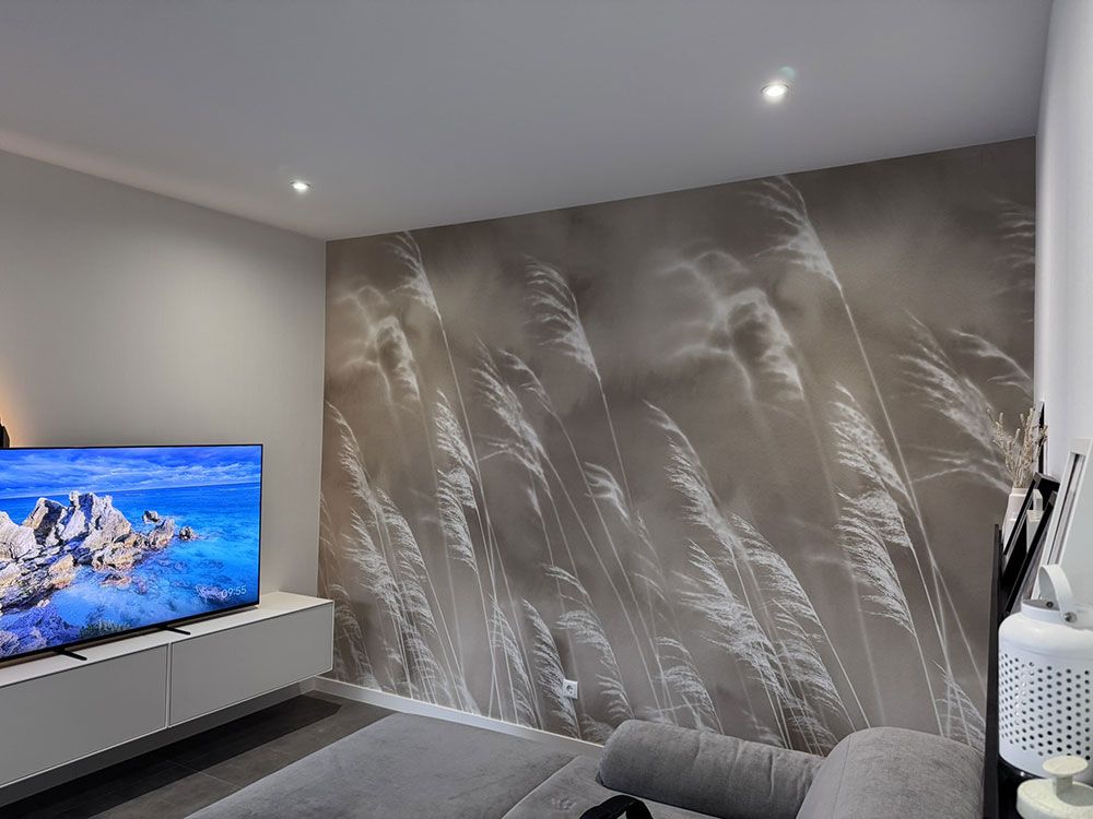 Wohnzimmer mit großem Fernseher, einer Wand in neutralen Tönen mit einem Weizenmotiv und einem grauen Sofa.