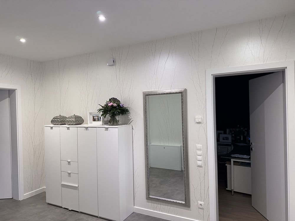 Weißer Flur mit einem Schrank, einem Spiegel und einer offenen Tür zu einem anderen Zimmer.