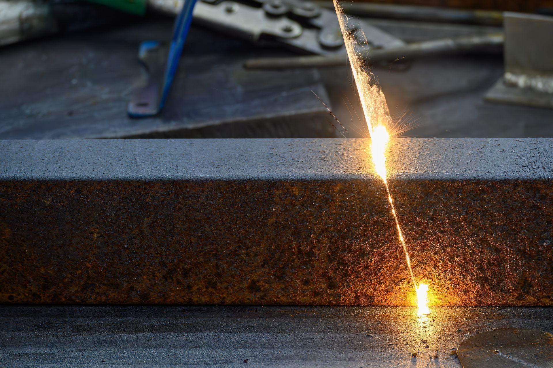 Vers la page Décapage fer/inox. Un laser décapant une poutre métallique rouillée, créant une ligne de lumière vive.