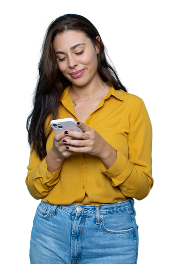 Une femme en chemise jaune et jean regarde son téléphone en souriant.