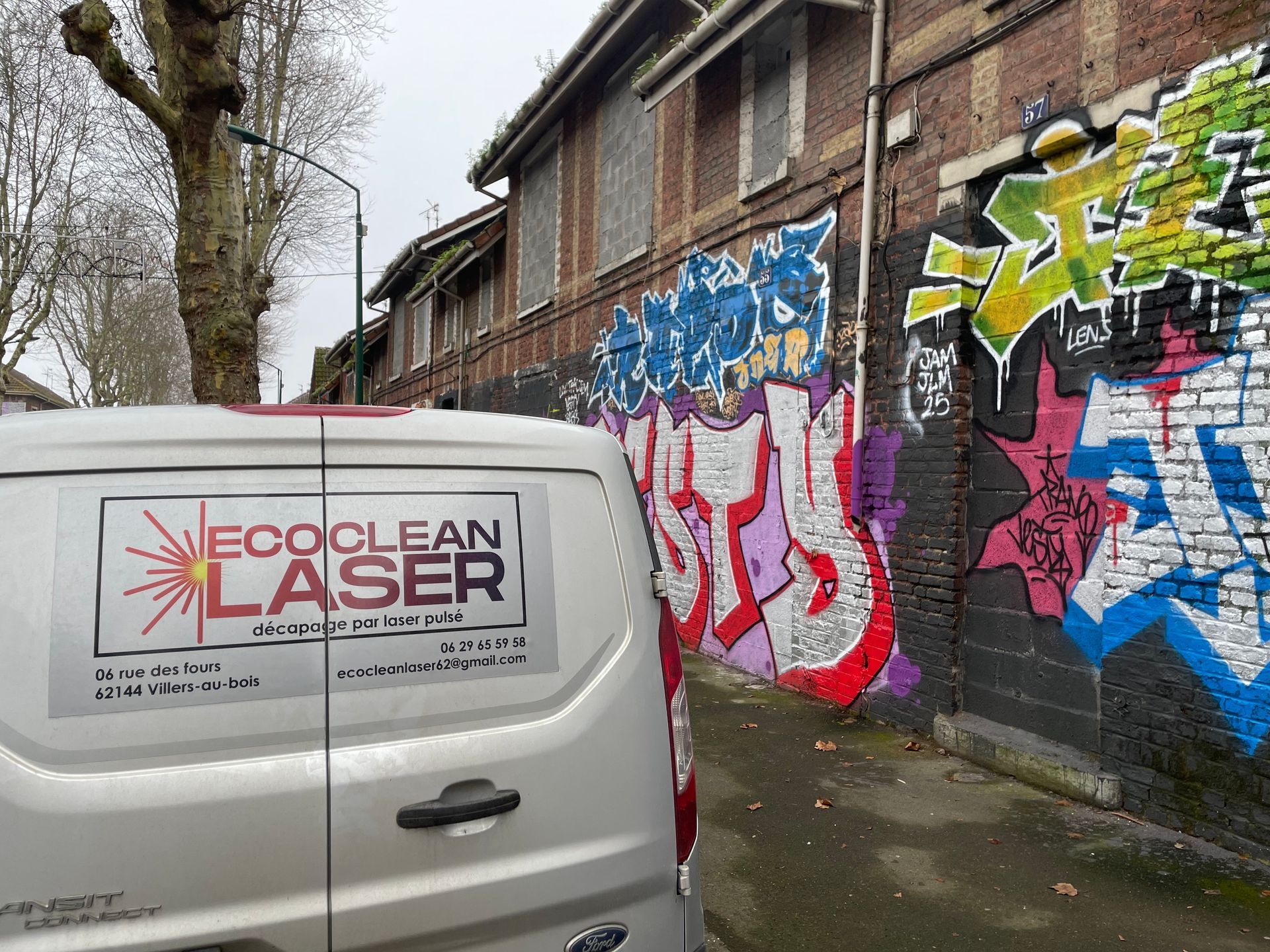 Une camionnette avec le logo Eco Clean Laser est garée près d'un mur de briques couvert de graffitis.