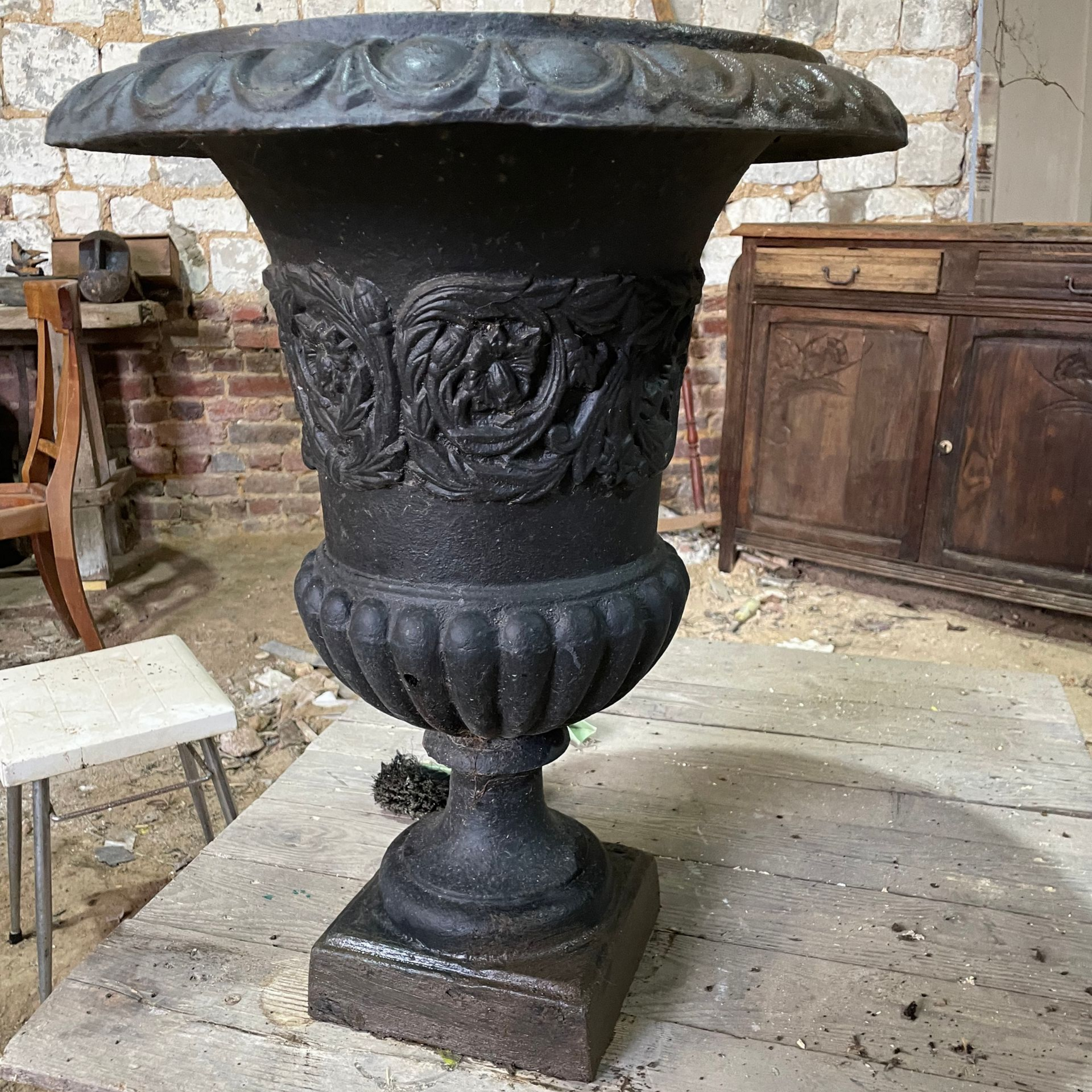 Urne en fonte noire ornée de motifs floraux, posée sur un socle carré.