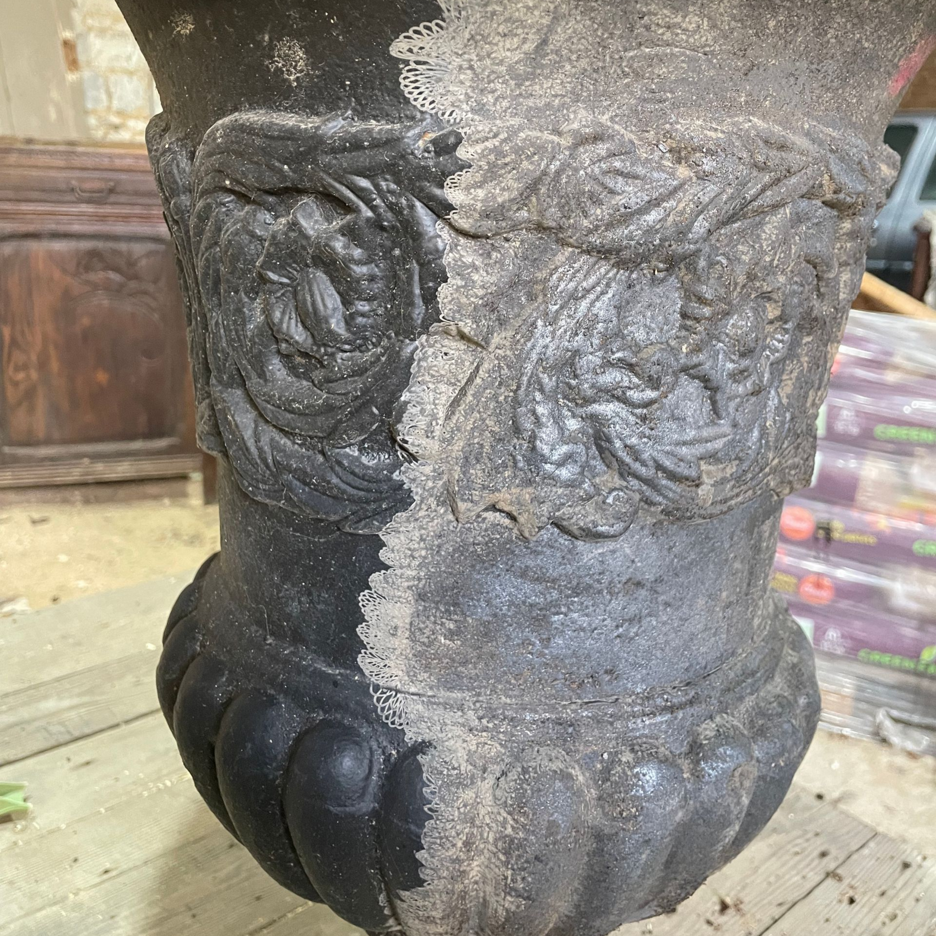 Gros plan sur une grande urne noire, partiellement nettoyée. On y distingue des détails ornementaux.