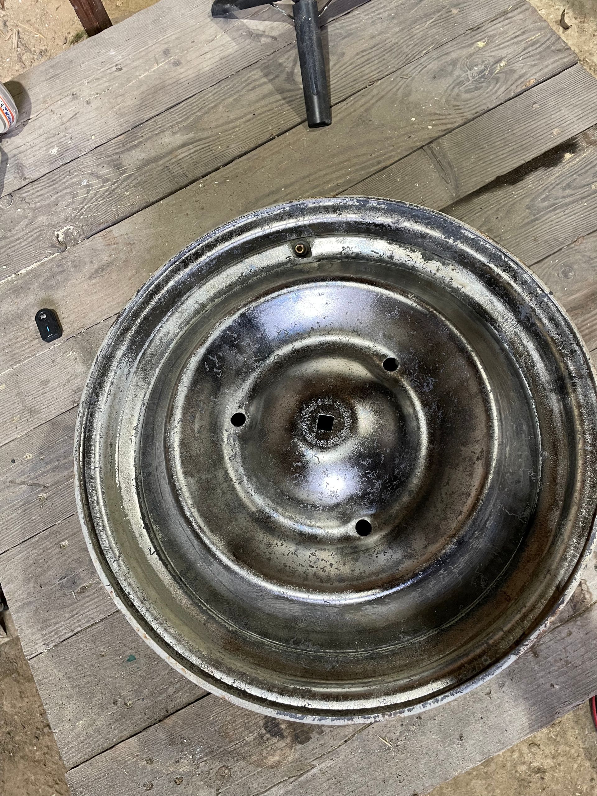 Roue métallique à moyeu central et trois trous, reposant sur des planches de bois.
