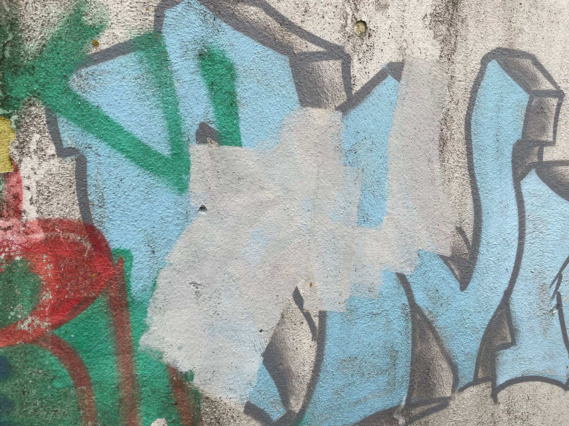 Graffiti sur un mur en béton : peinture bleue, verte et rouge avec une tache grise où la peinture a été enlevée.