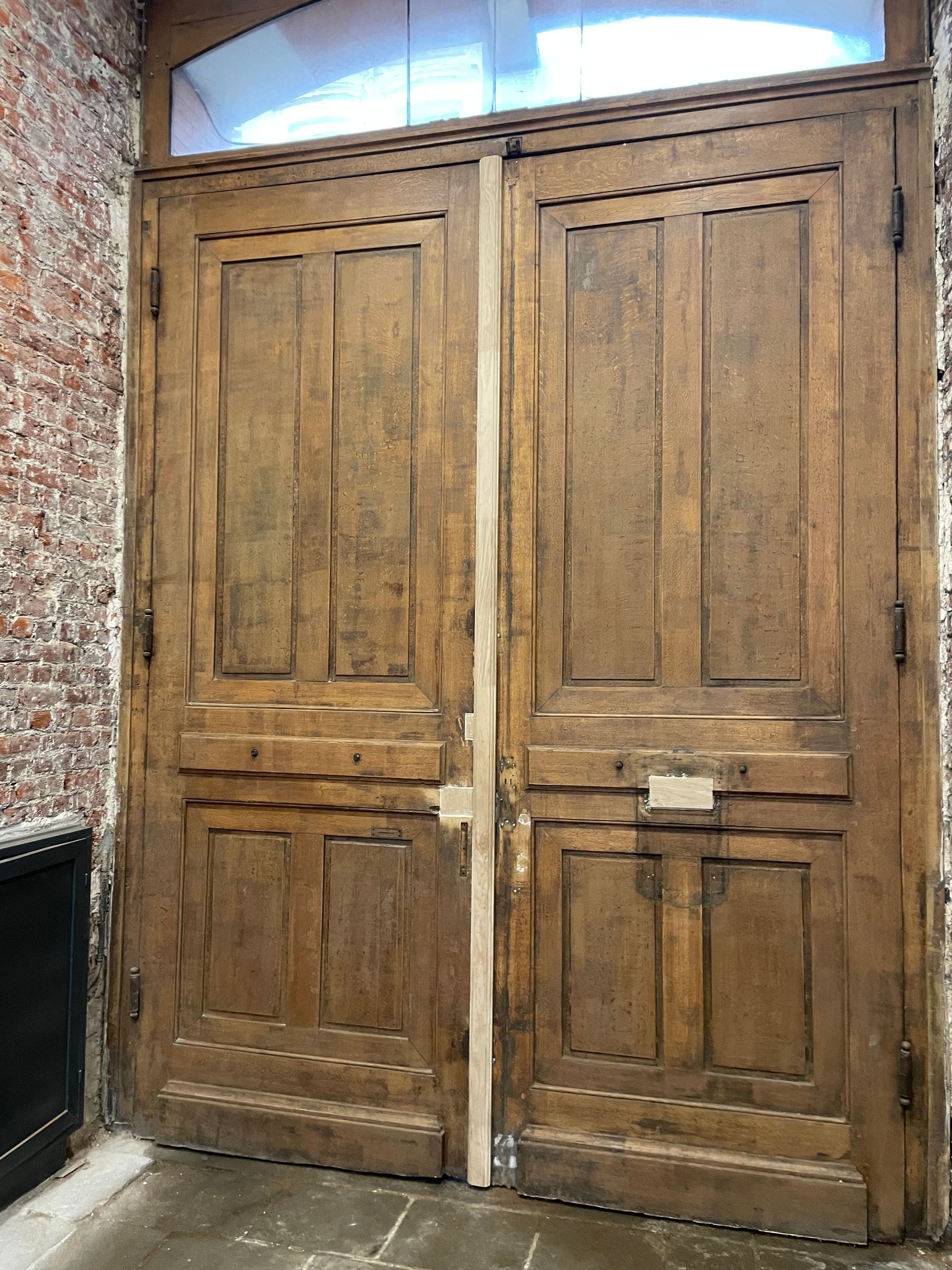 Double porte en bois à l'aspect vieilli ; mur de briques sur le côté.