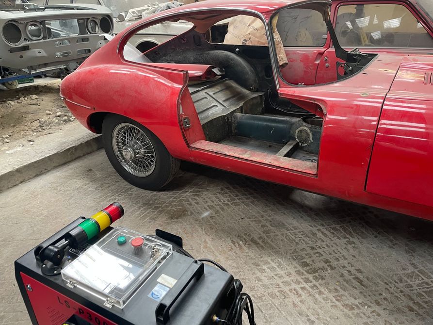 Une voiture ancienne rouge est en cours de restauration dans un atelier.