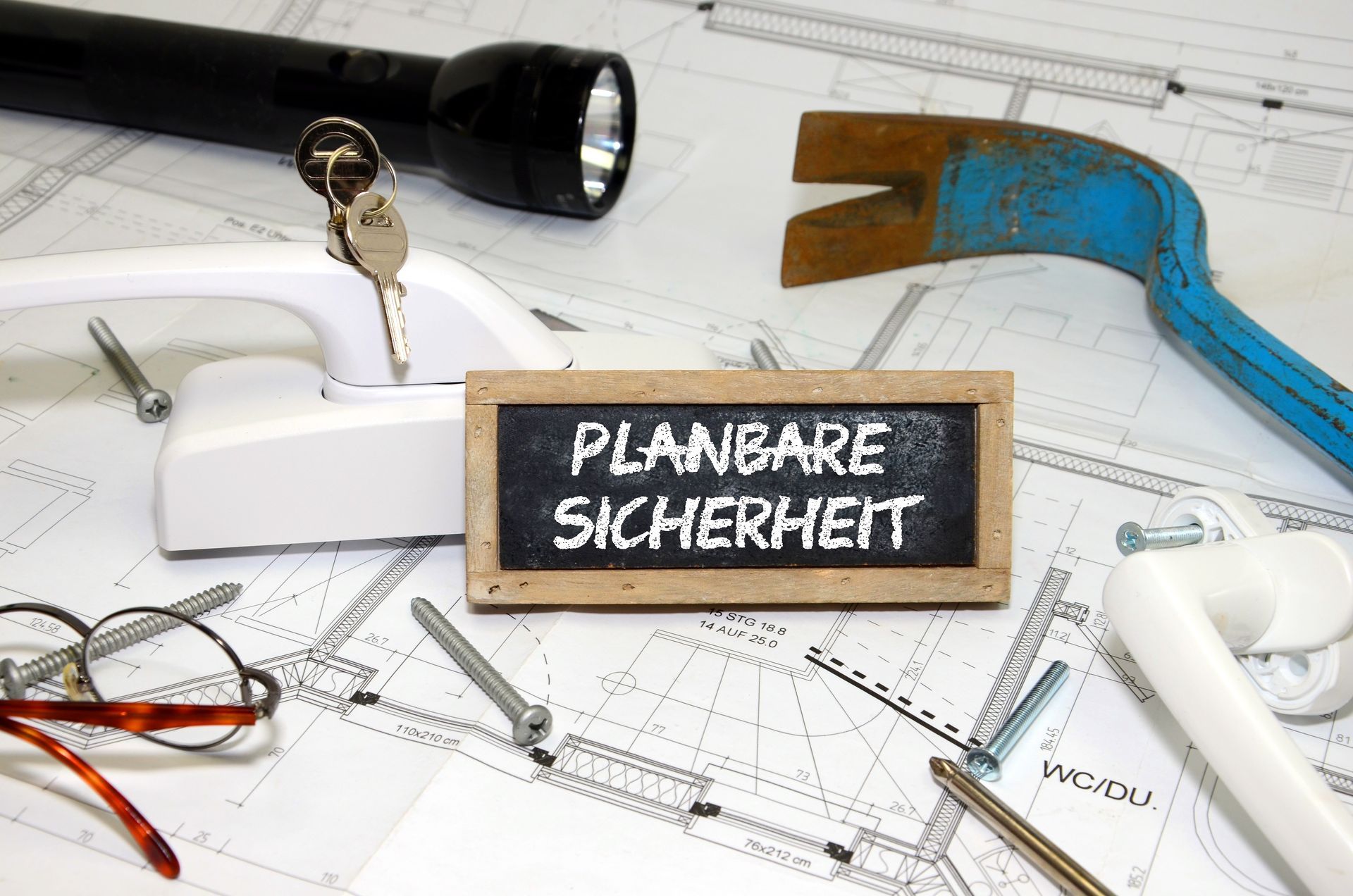 Bauplanskizze, darauf verteilt eine Taschenlampe, eine Brille, Fenstergriff mit Schlüssel 