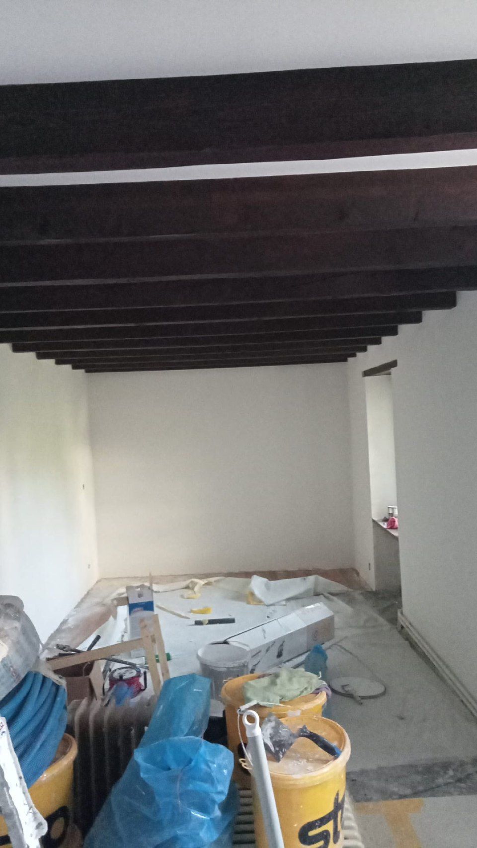 Une pièce avec des poutres en bois et des seaux de peinture.