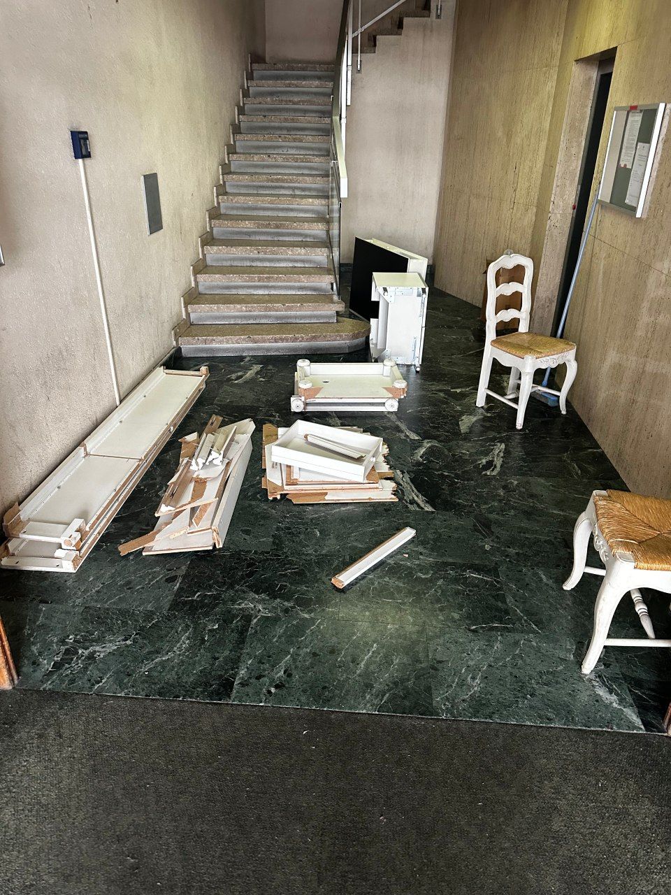 Une pièce avec des escaliers, des chaises et des caisses au sol.