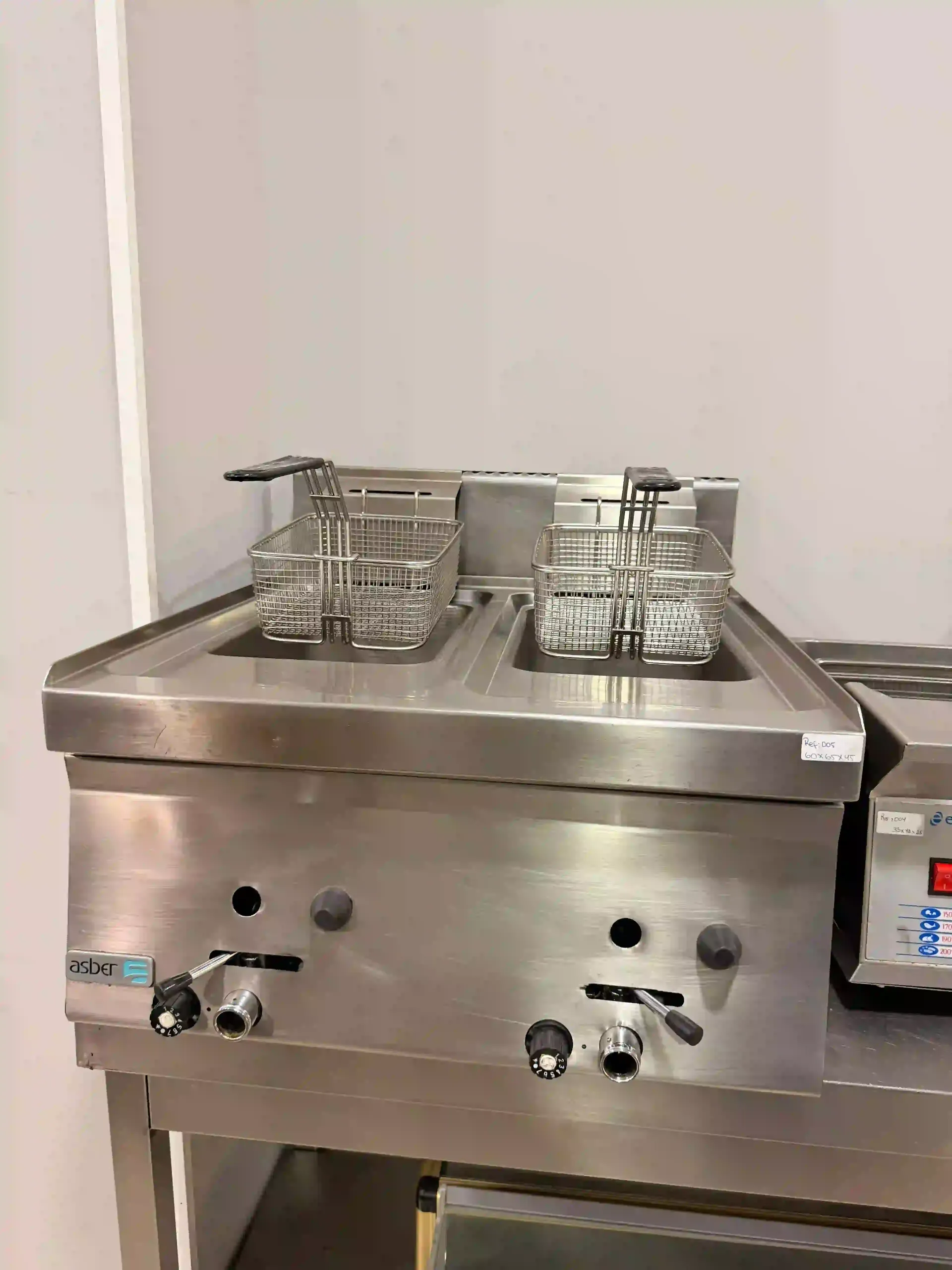 Freidora de acero inoxidable de sobremesa con dos cestas de alambre y mandos de control sobre una encimera de cocina.