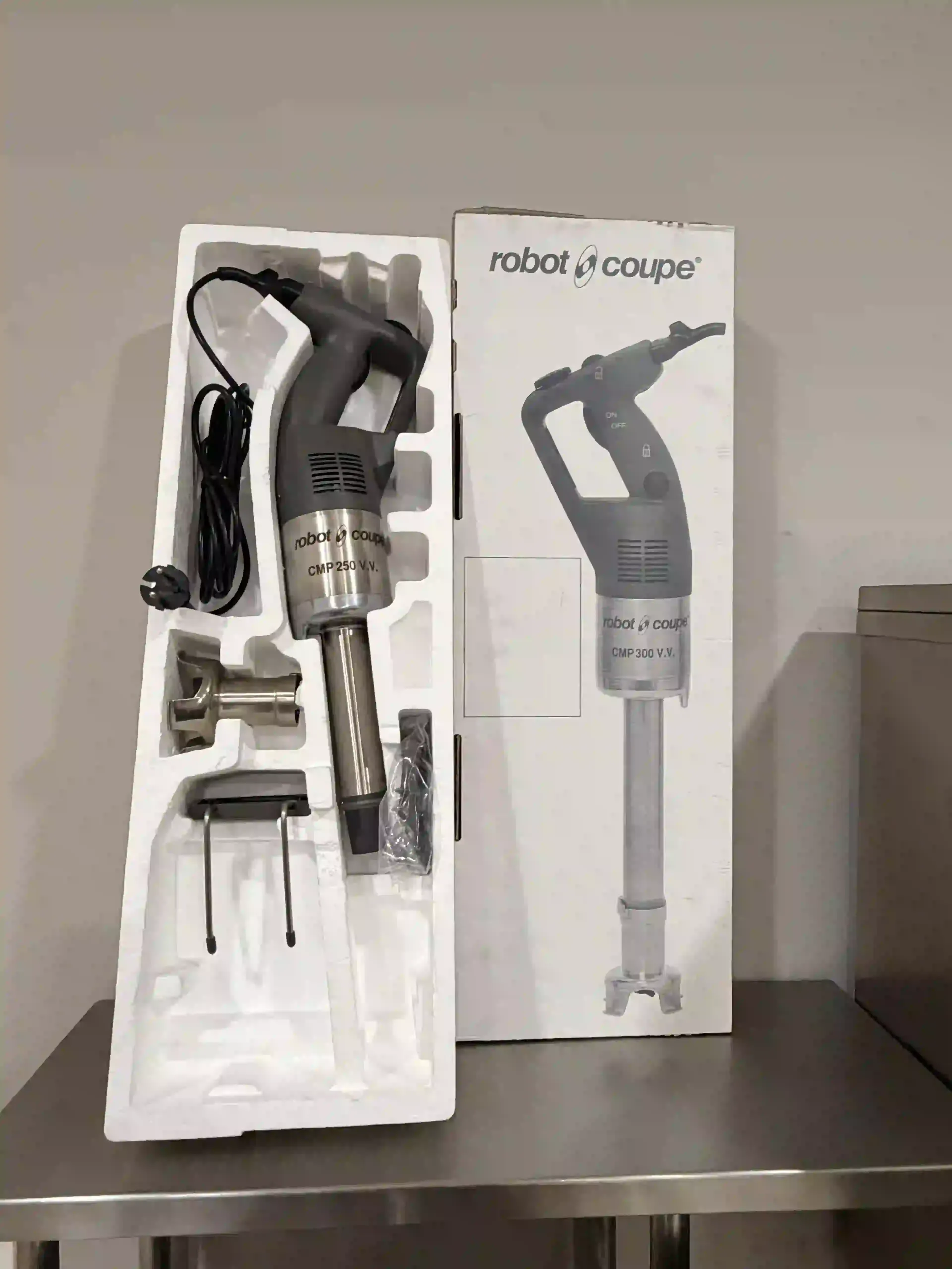 Batidora de mano Robot Coupe en caja sobre una mesa de metal, con el mango, los accesorios y el soporte a la vista.