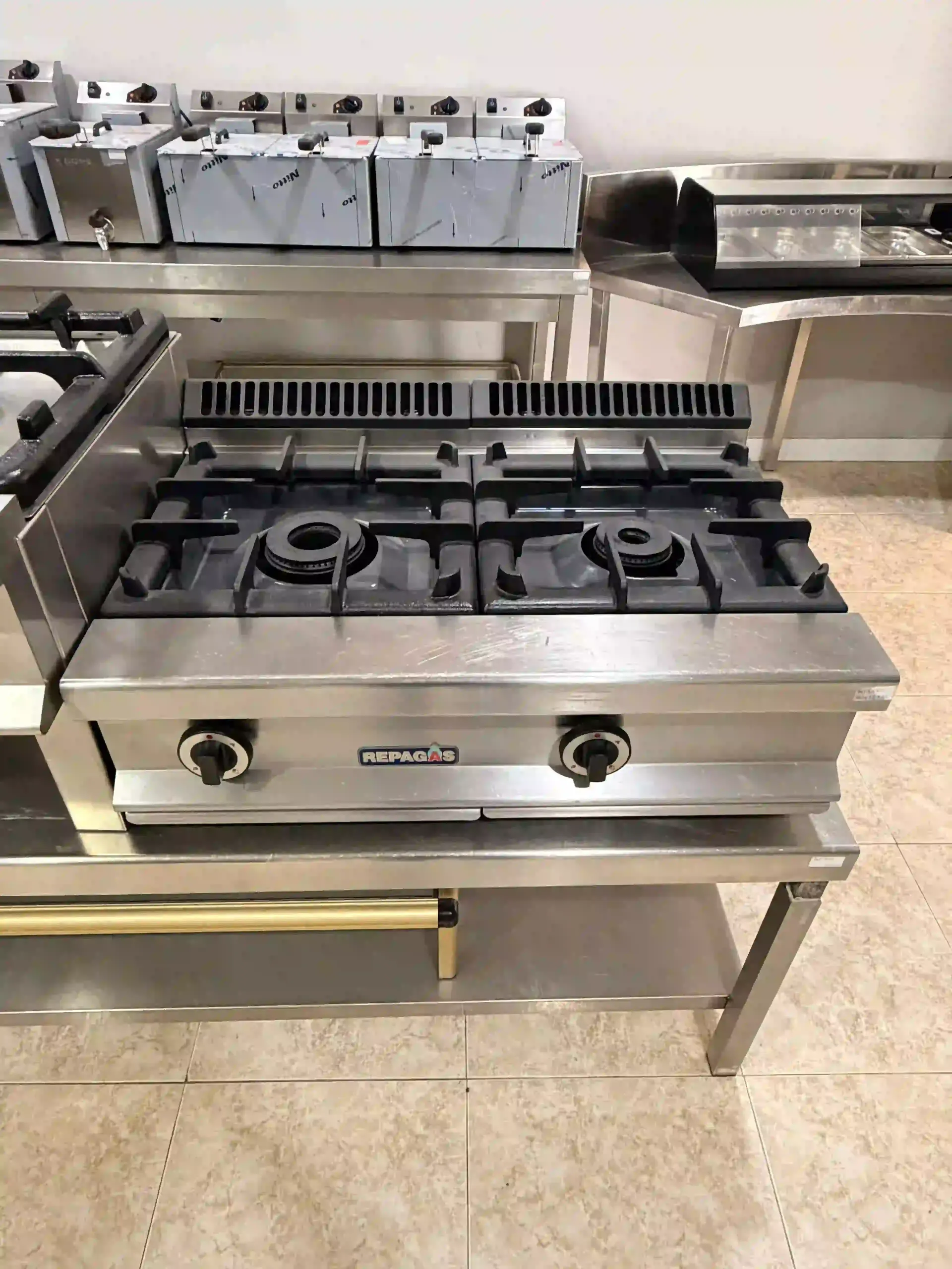 Cocina industrial con estufa de gas de acero inoxidable, cuatro quemadores y horno.