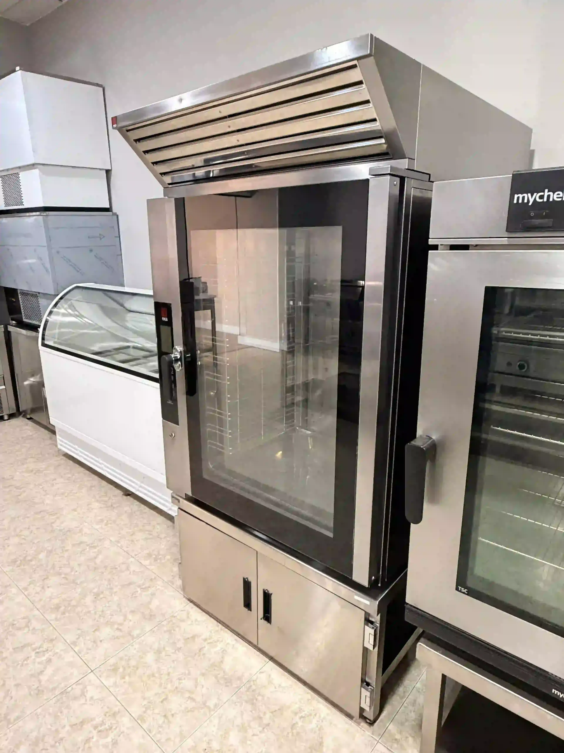 Refrigerador comercial con puerta de vidrio en un pasillo de tienda, de acero inoxidable con detalles en negro.