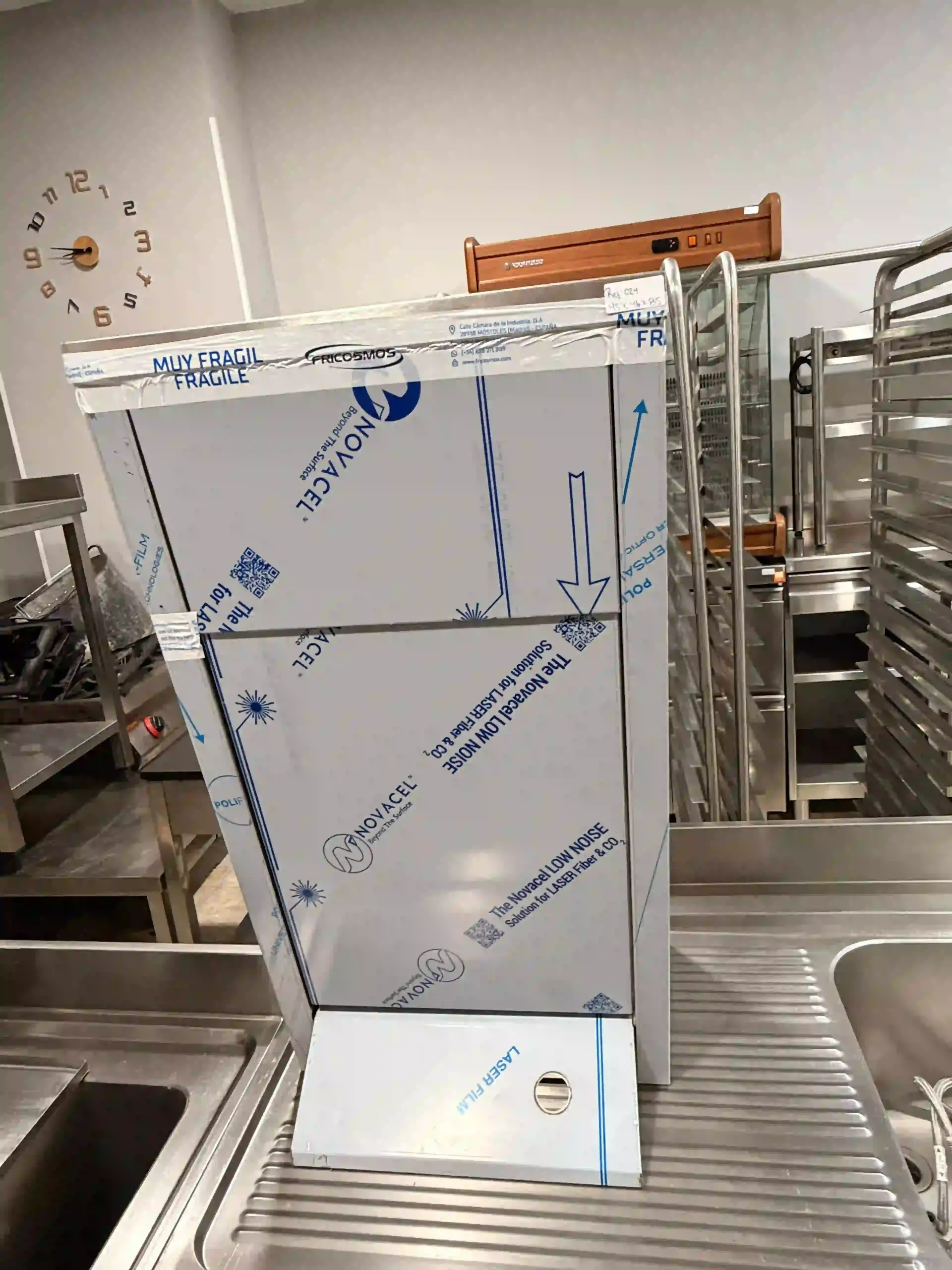 Electrodoméstico de acero inoxidable envuelto en una cocina comercial cerca de fregaderos y estantes metálicos.