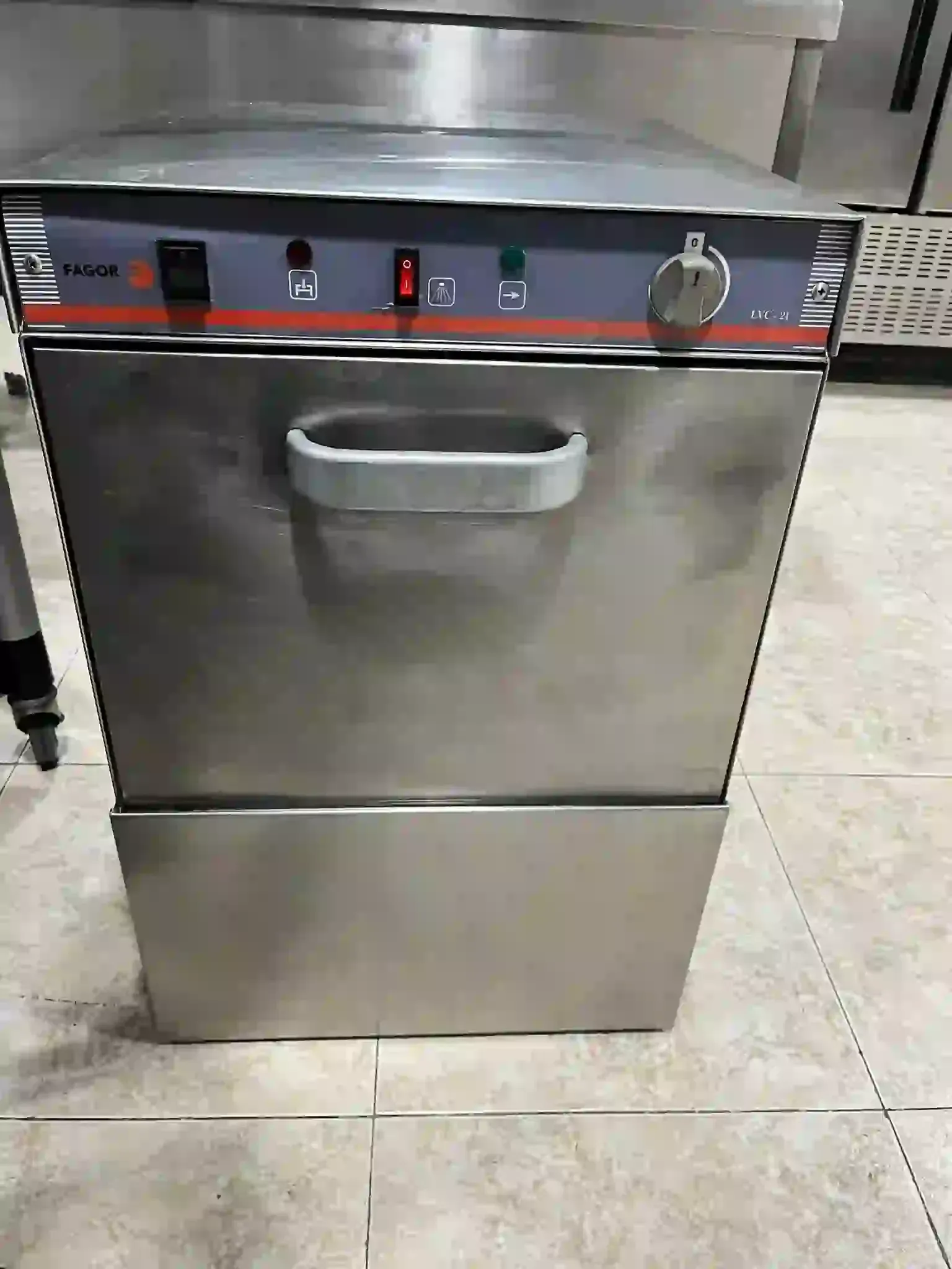 Lavavajillas comercial de acero inoxidable con tirador frontal en una zona de cocina alicatada