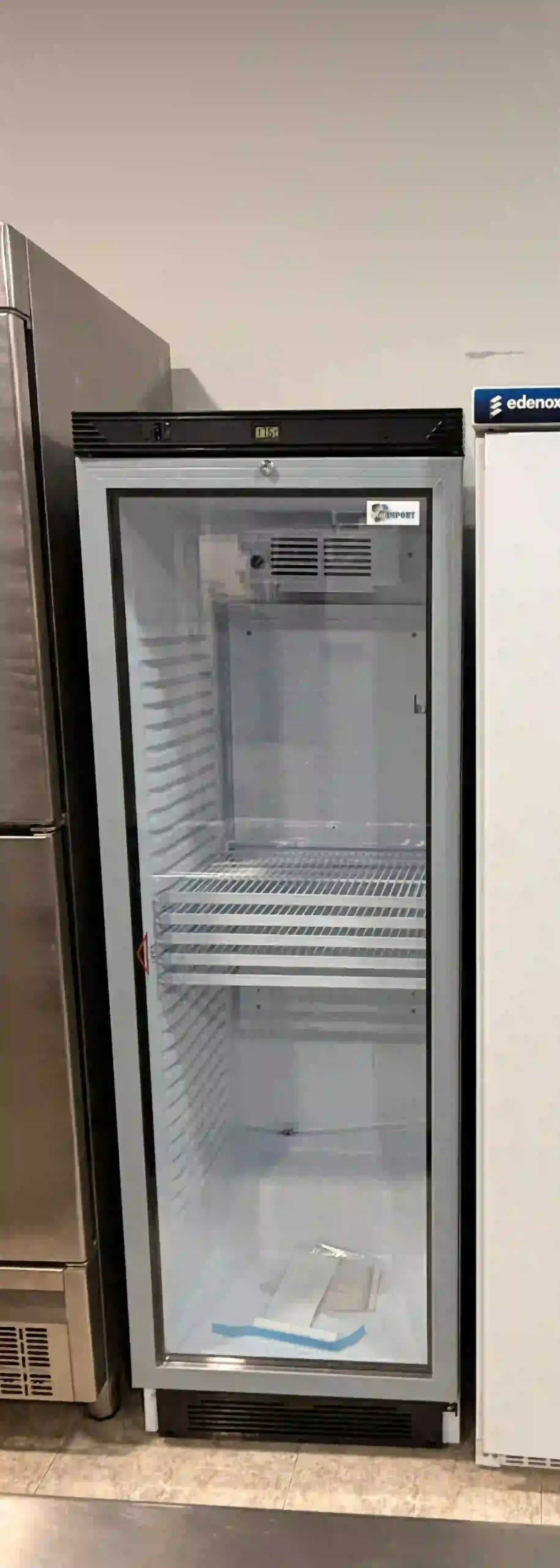 Refrigerador de bebidas vacío con puerta de vidrio en el pasillo de una tienda, con estantes visibles en el interior.