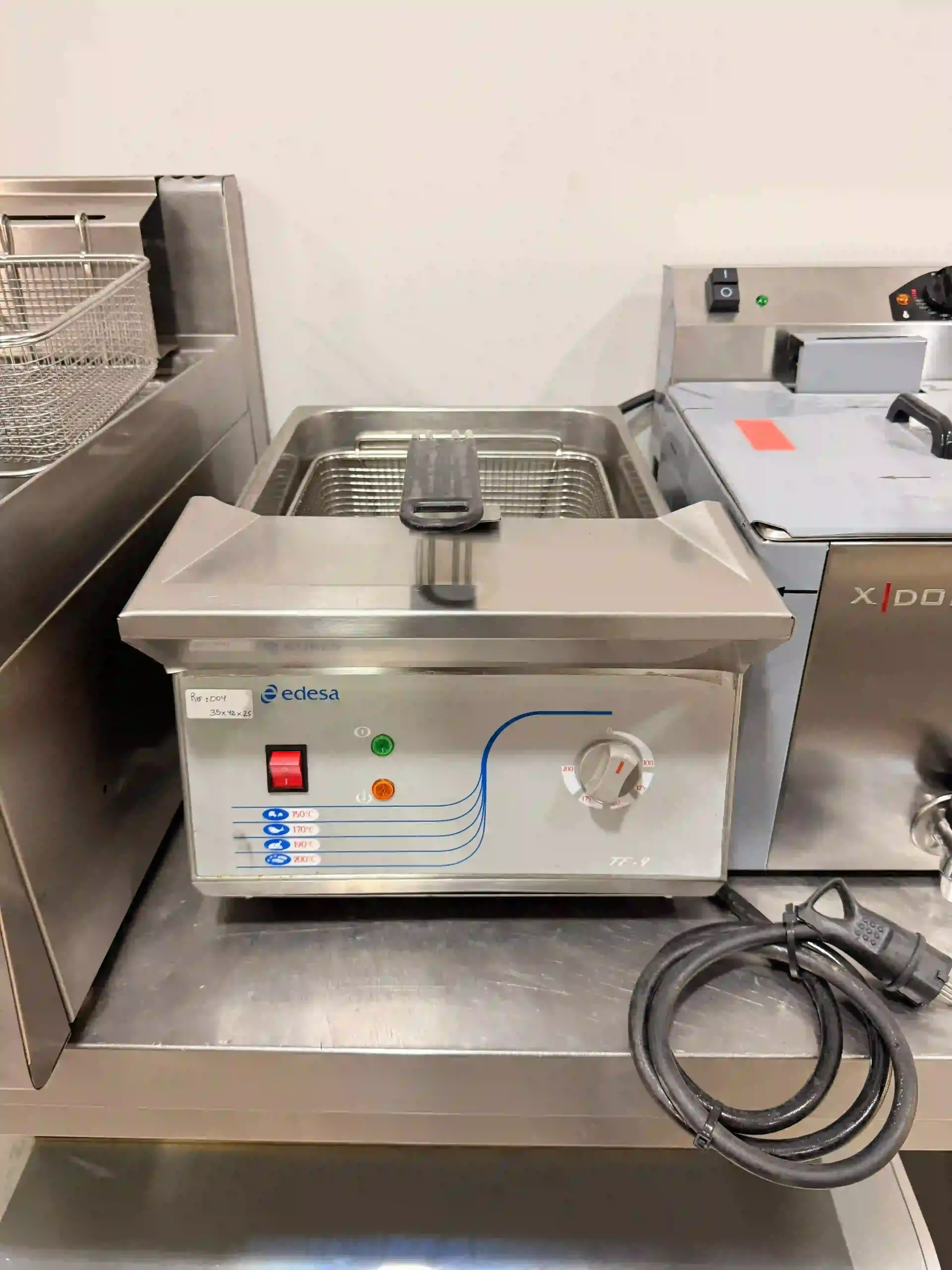 Freidora de encimera de acero inoxidable en una cocina comercial, con un cable de alimentación enrollado al lado.
