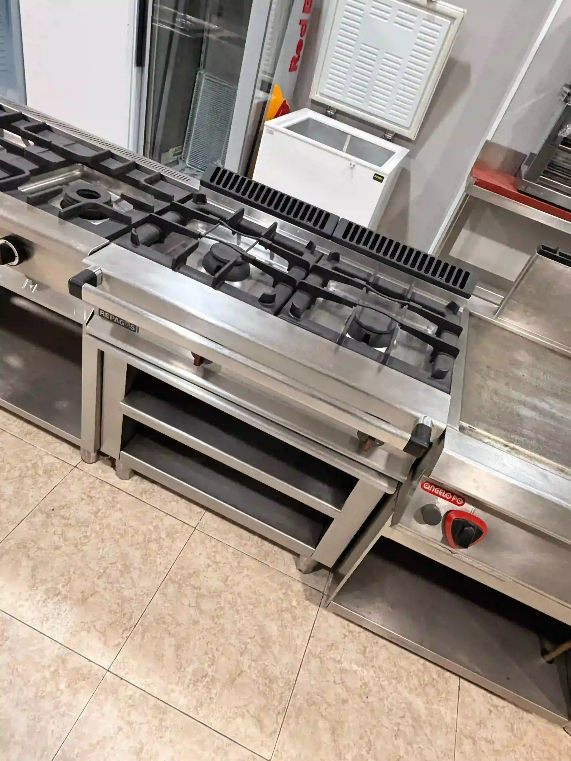 Cocina de gas comercial con horno en la cocina de un restaurante, de acero inoxidable y quemadores negros.