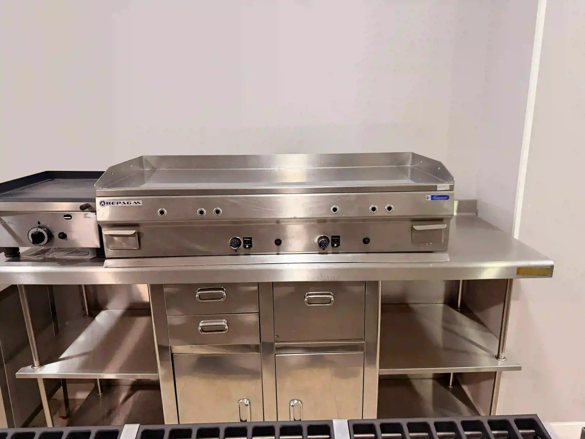 Parrilla de cocina comercial de acero inoxidable sobre una encimera de preparación con cajones y estantes debajo.