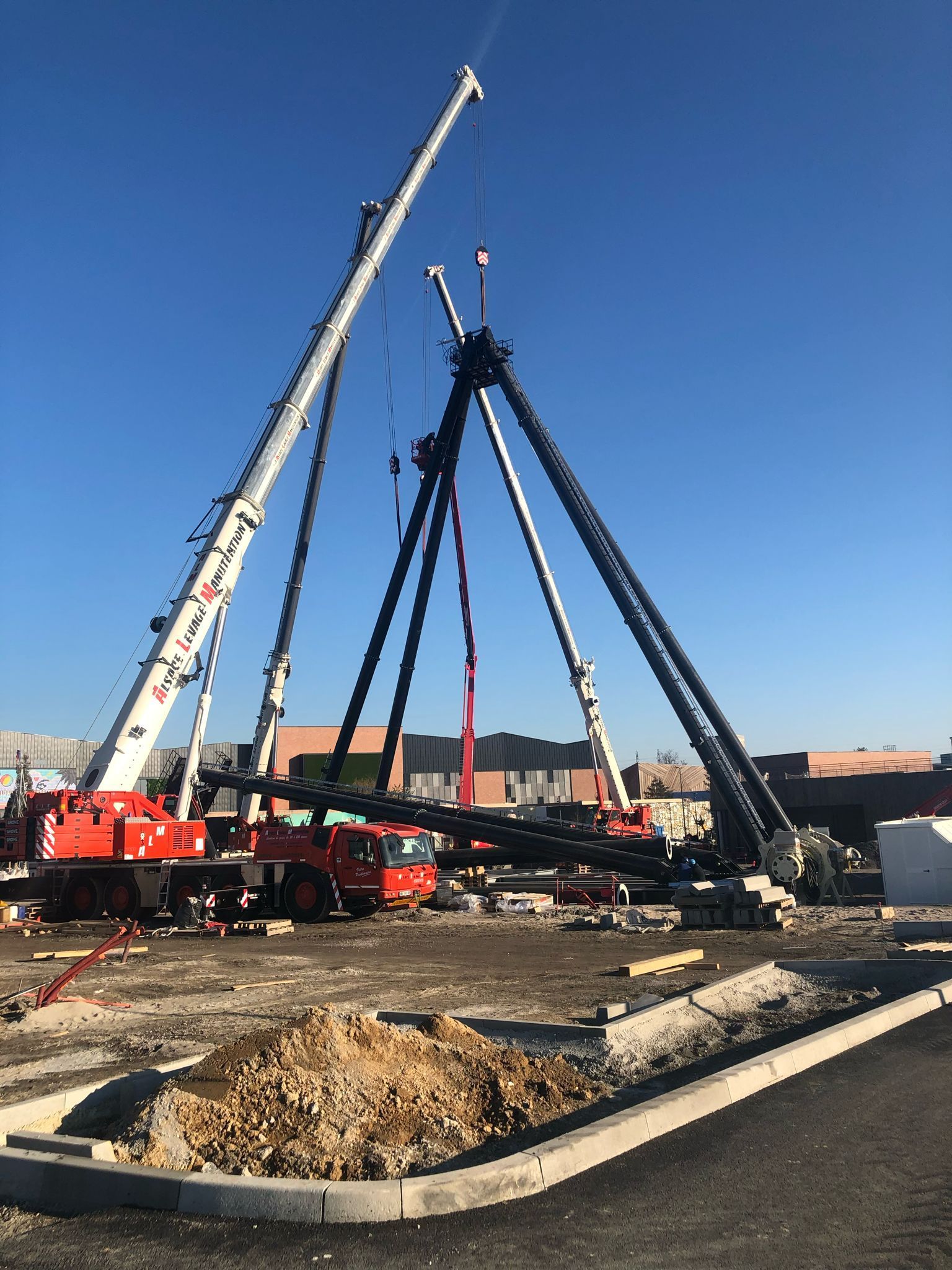 Plusieurs camions grues levant une grosse structure métallique