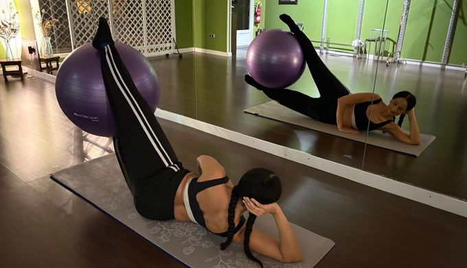 Mujer haciendo ejercicio con una pelota en un estudio, con la pierna levantada. 