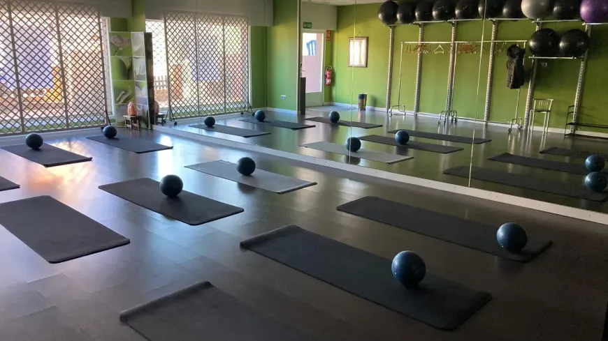 Estudio de pilates con colchonetas, pelotas y espejos grandes. Paredes verdes e iluminación brillante.