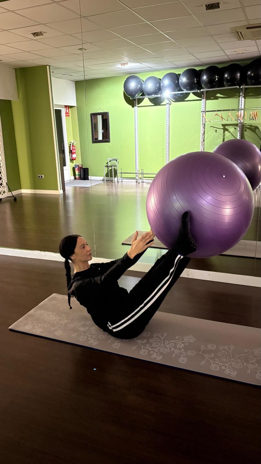Mujer vestida de negro para hacer ejercicio haciendo ejercicios abdominales con una pelota 