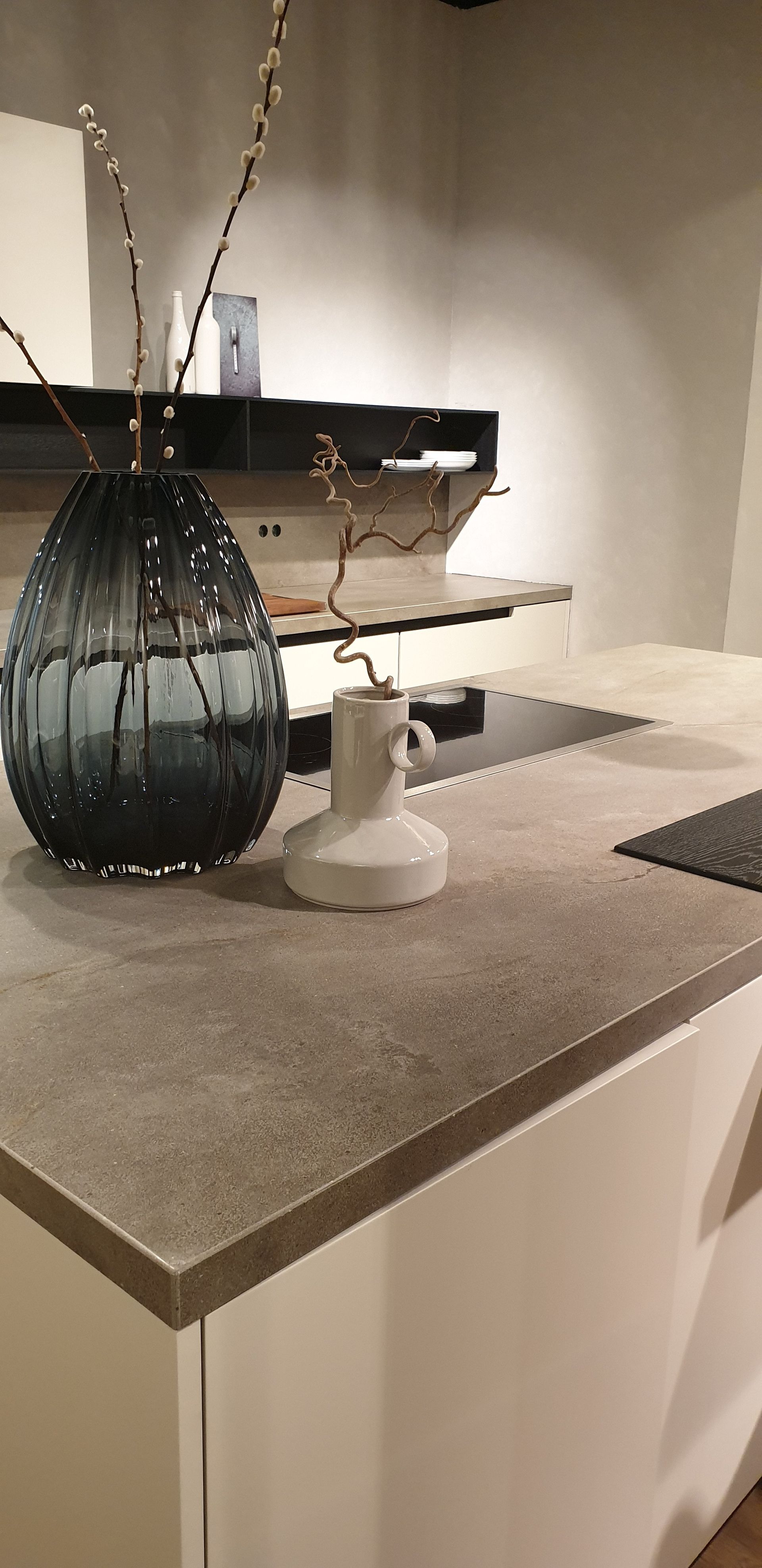 Una encimera de cocina moderna con un jarrón, flores y una pequeña pieza decorativa blanca.