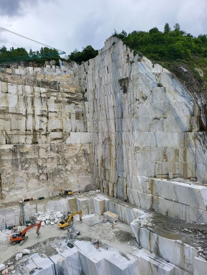 Cantera de mármol a cielo abierto con altos muros de piedra blanca y maquinaria en la base, bajo un cielo nublado.