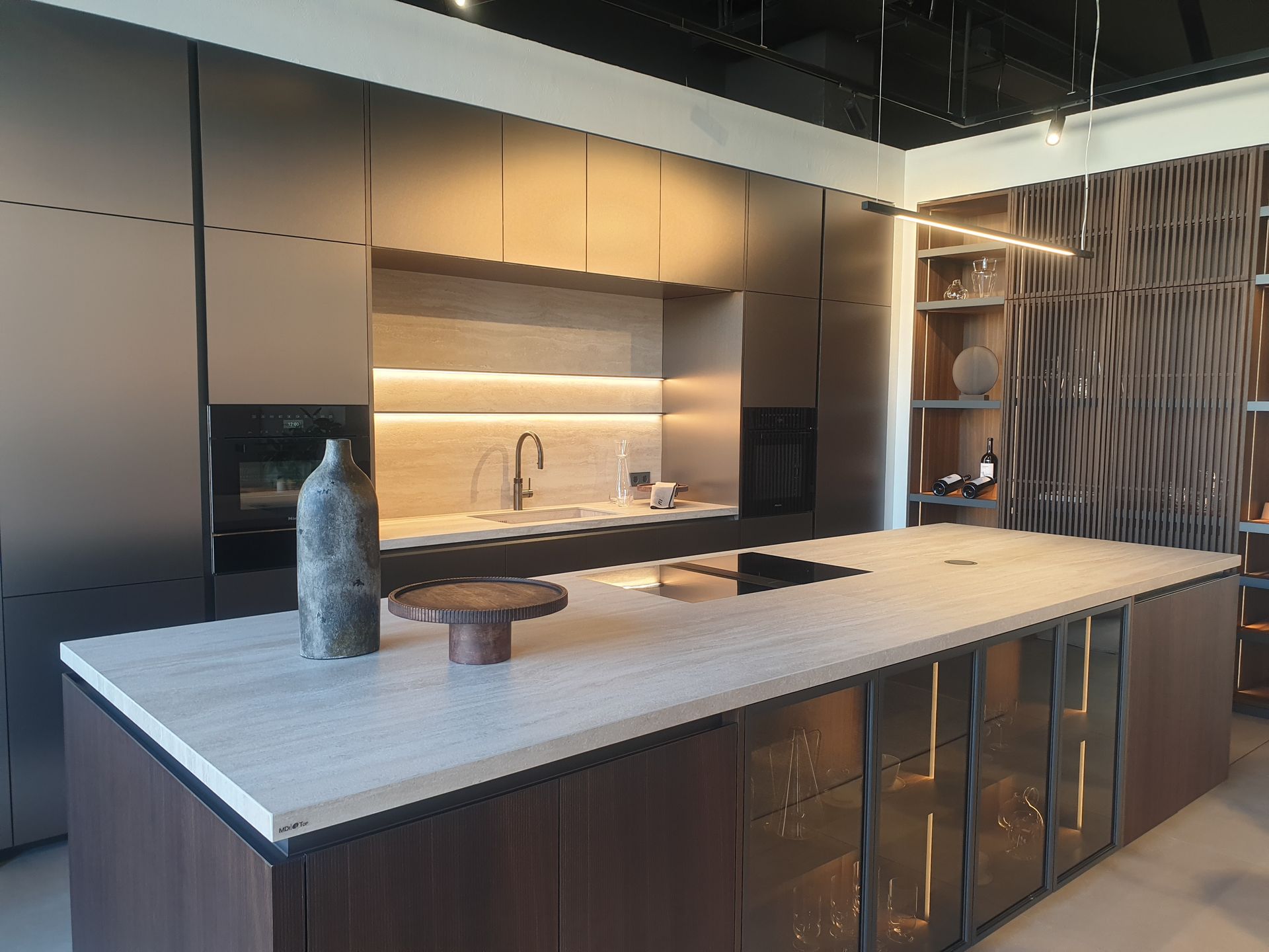 Cocina moderna con gran isla y muebles oscuros; tonos neutros con iluminación cálida.