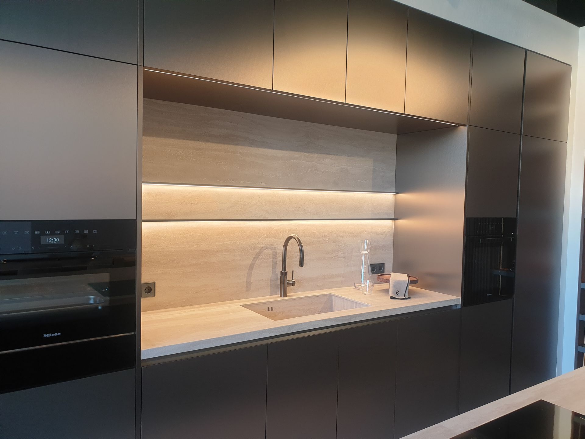 Cocina moderna con gabinetes gris oscuro, fregadero empotrado e iluminación cálida.