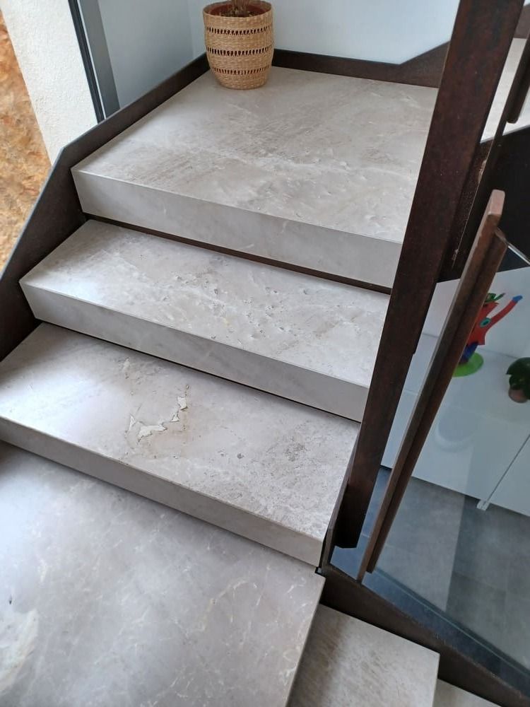 Escaleras de piedra con barandilla de metal oscuro, ambiente interior.