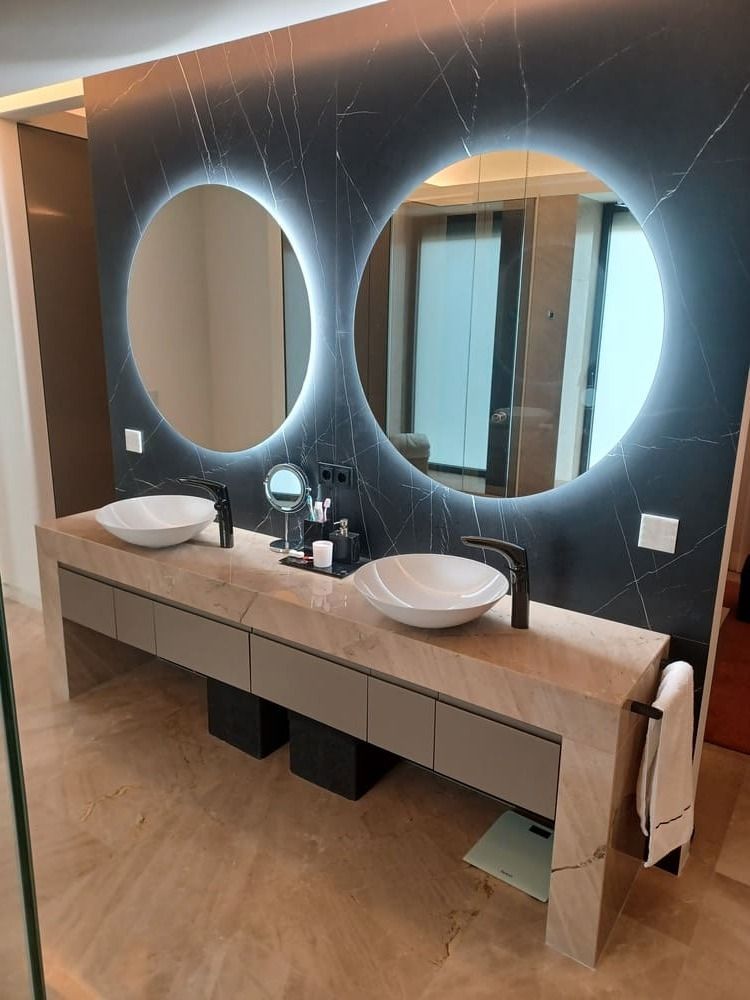 Baño moderno con dos espejos redondos, un tocador doble y una pared decorativa negra.