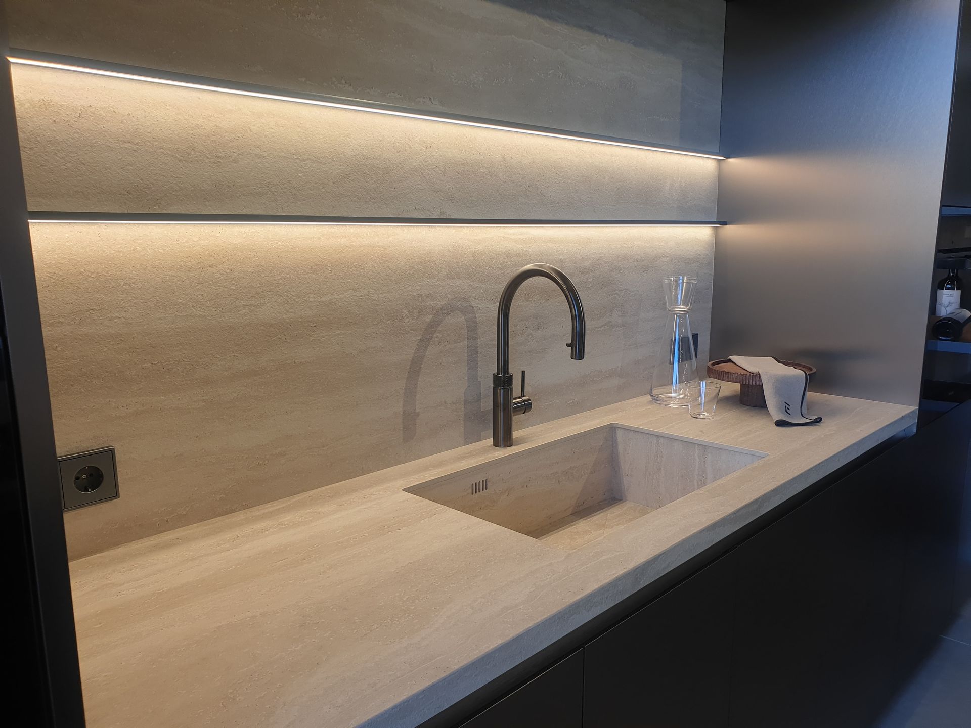 Fregadero de cocina moderno con encimera de piedra, grifo e iluminación debajo del gabinete.