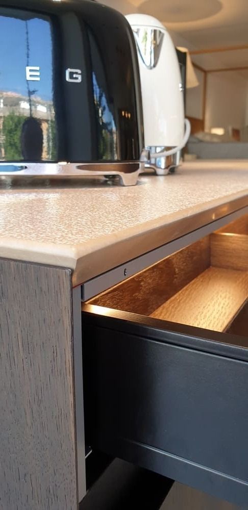 Tostadora negra y tetera blanca sobre una encimera con un cajón abierto, probablemente un entorno de cocina.