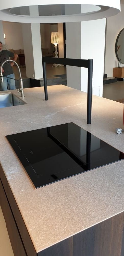 Isla de cocina moderna con anafe negro, ventilación incorporada y encimera de color claro.