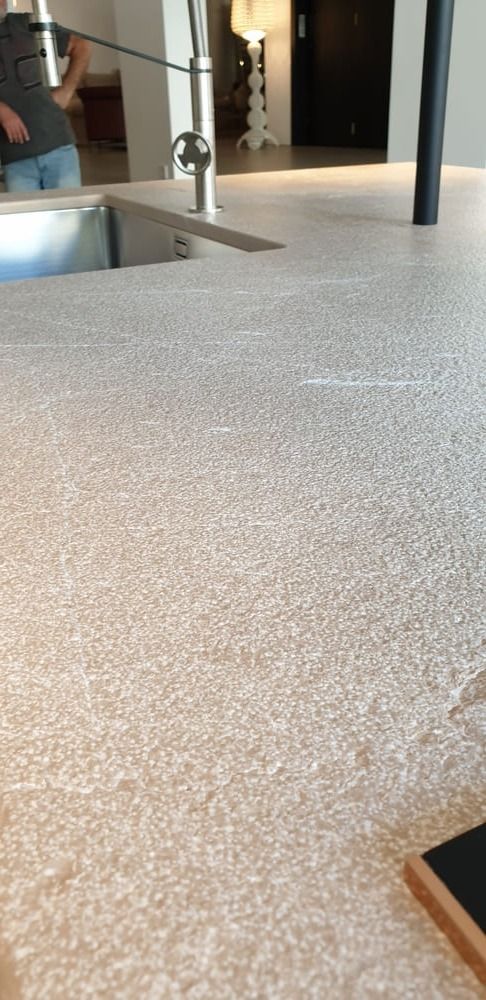 Primer plano de una encimera moteada clara con un fregadero, un grifo y una persona en el fondo.