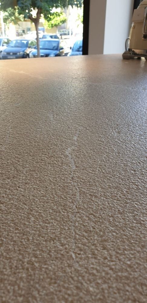 Un primer plano de una superficie texturizada de color beige con una ligera costura, frente a una ventana con automóviles y árboles visibles.