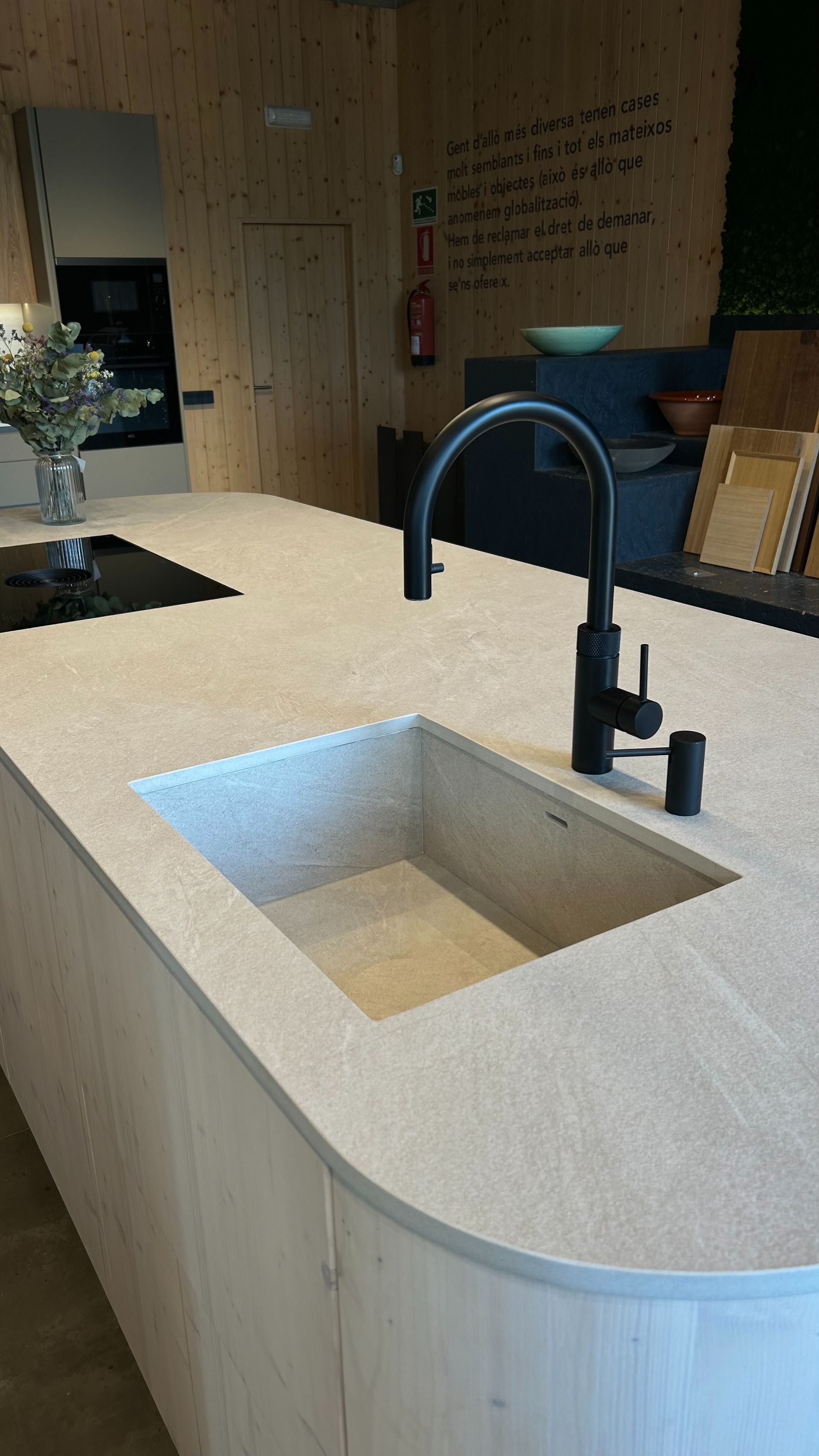 Isla de cocina con fregadero integrado y grifo negro. Gabinetes y encimera de madera clara.