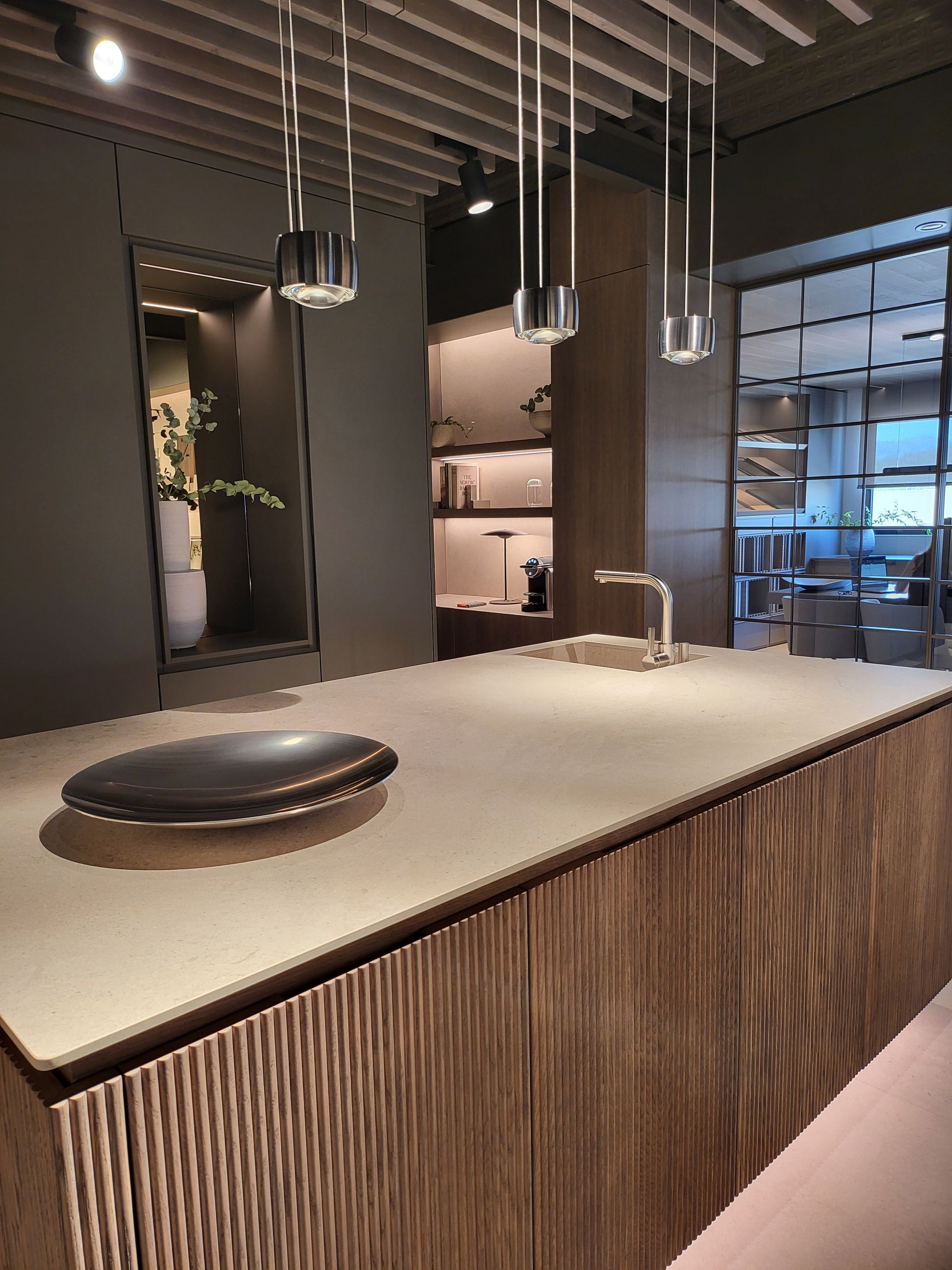 Isla de cocina moderna con gabinetes de veta de madera, encimera de concreto y luces colgantes.