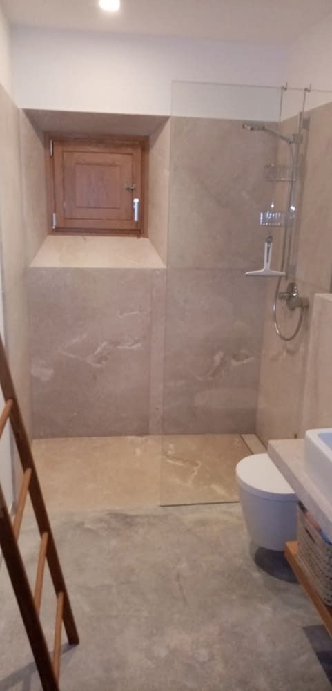 Baño con ventana, ducha, inodoro y escalera. Colores neutros y suelo de hormigón sin acabar.