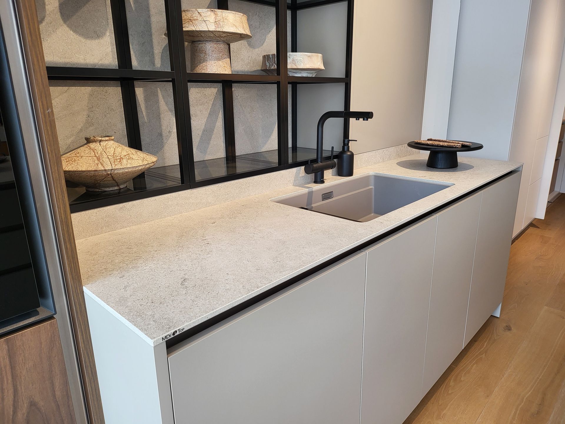 Isla de cocina moderna con encimera gris claro, fregadero, grifo negro y gabinetes.