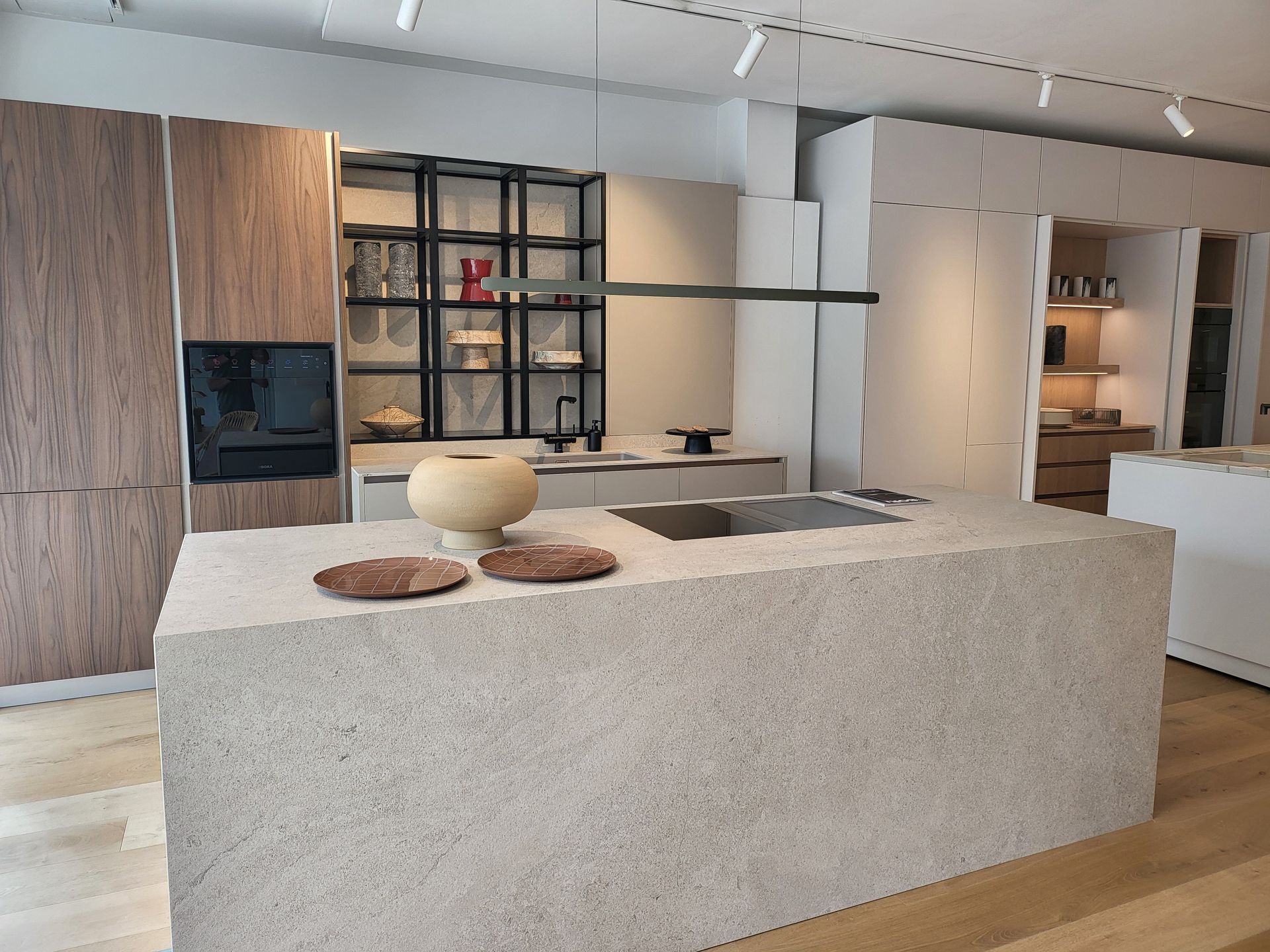 Cocina moderna con gran isla de piedra, gabinetes de madera y detalles en negro.