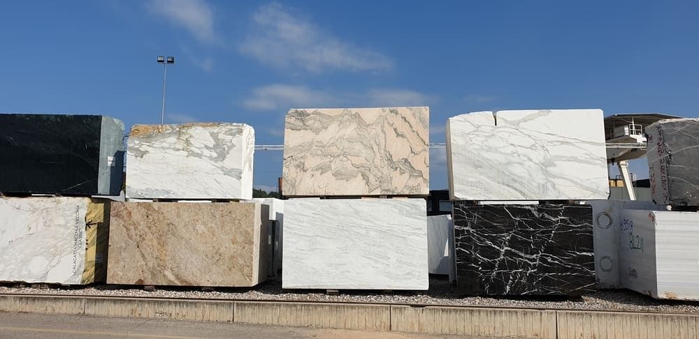 Bloques de mármol de varios colores apilados al aire libre contra un cielo azul.