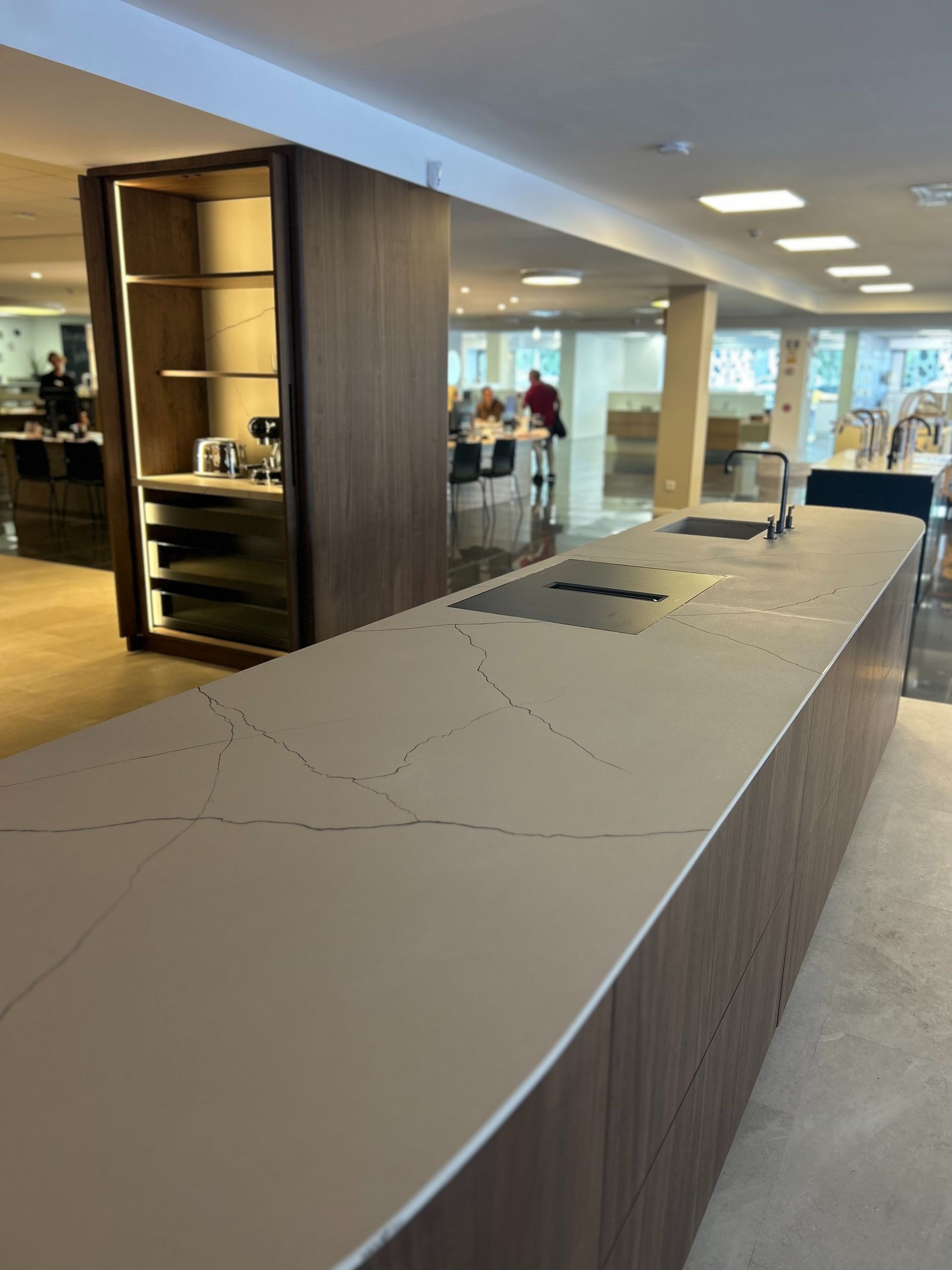 Isla de cocina con encimera gris y gabinetes de madera oscura, electrodomésticos y estantes abiertos.