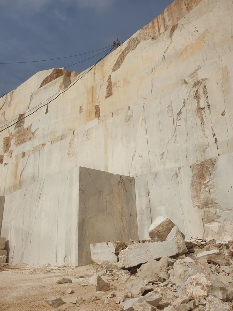 Una gran cantera de piedra blanca con un enorme bloque cuadrado al frente. Escombros dispersos en primer plano.