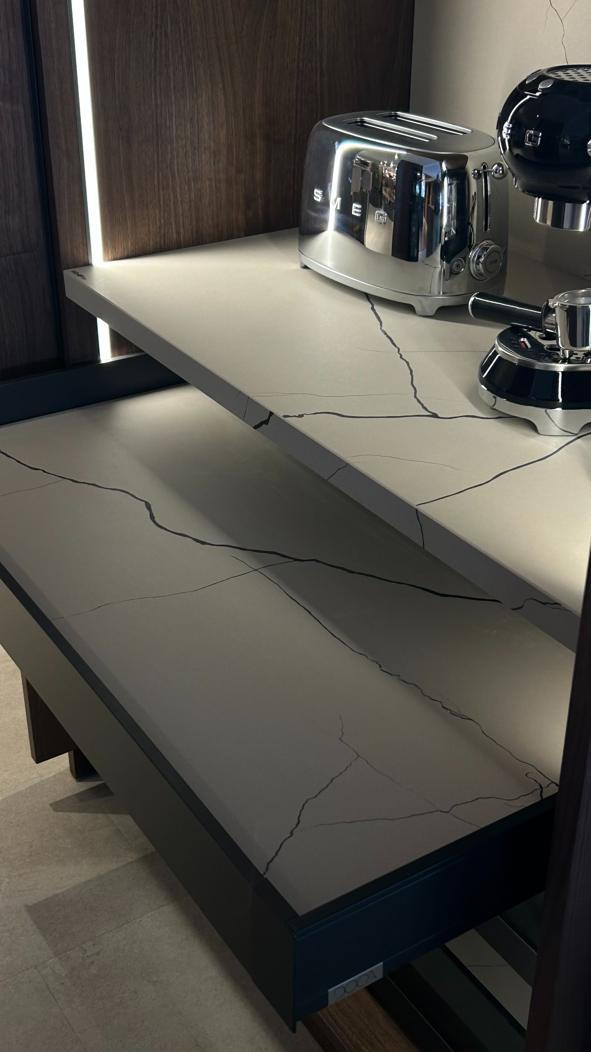 Estantería de dos niveles con encimeras blancas y vetas negras, que contiene una tostadora y una máquina de café expreso.